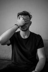 Black and White, Young white man wearing a black t-shirt standing over green background with hand on face covering eyes. Blind concept.