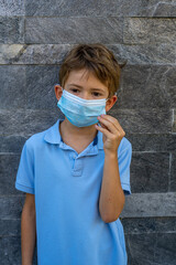 A boy in a blue t-shirt, wearing a medical mask against a background of coronovirus on a grey background. A child in a mask.