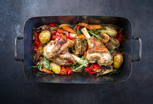 Traditional braised leg of lamb with eggplant, potatoes and tomatoes offered as top view in a rustic old roasting dish .