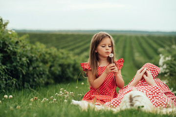 Young Mom with her Little Daughter Dressed Alike in Red Polka Dot Dress, Having Fun Time in the Field Outside the City, Motherhood and Childhood Concept