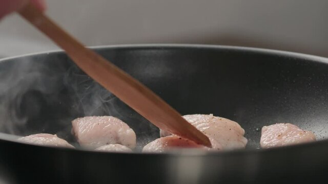 Slow motion turn over chicken fillet slices on non-stick pan with wooden spatula closeup
