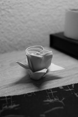Origami rose made of white paper placed on a wooden table AM
