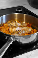 Chicken drumsticks covered in rosemary with tagliatelle pasta and tomato sauce.  Cooking on a hob stove in a frying pan.