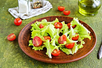 Fresh salad with, lettuce and cherry tomatoes on a brown clay plate on an olive concrete background.