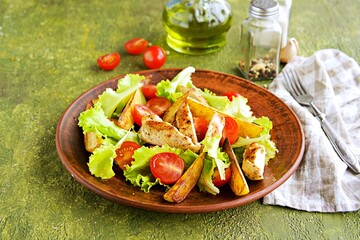 Warm salad with fried chicken fillet, lettuce and cherry tomatoes on a brown clay plate on an olive concrete background.
