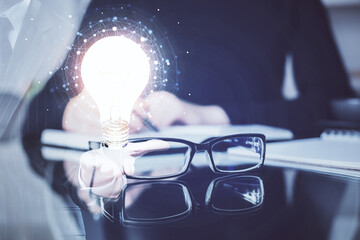 Bulb hologram over hands taking notes background. Concept of idea. Double exposure