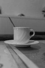 Small white ceramic coffee cup with a handle and a spoon placed on a white ceramic plate on a table
