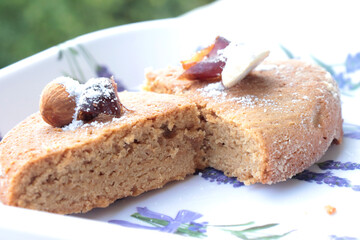 Indian home baked egg less spongy floor and coffee flavored cake called atta cake garnished with almond, cashew and Arabian dates in a lavender white plate