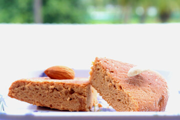 Indian home baked egg less spongy floor and coffee flavored cake called atta cake garnished with almond, cashew and Arabian dates in a lavender white plate