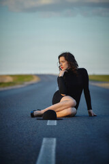 attractive girl in black dress and hat posing on the road with a dividing strip