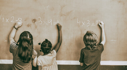 Three multi ethnic school pupils at the classroom chalkboard, back view. Back to school concept