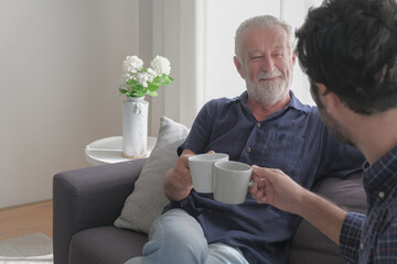 Happy smile old caucasian man drinking coffee with son in living room house.