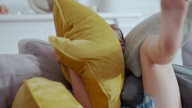 Cute young caucasian blonde girl preschool daughter playing with soft large pillows on bed in the room. Carefree childhood. Emotions. Young people. Activity.