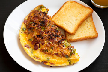 Homemade Denver Omelette on a white plate on a black background, side view.