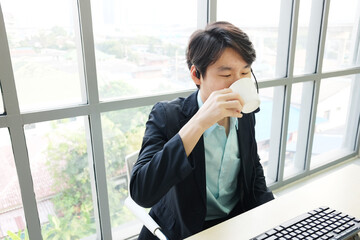 Businessman Call Center and technical Support staff with headset is drinking Coffee at computer desk. Asian customer support team.