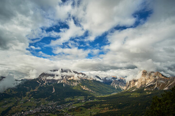 A panoramic landscape view of clouds over The Dolomites mountain ranges overlooking an alpine valley below. A scenic view taken from Monte Cristallo near Cortina in Italy.