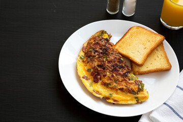 Homemade Denver Omelette on a white plate on a black background, side view. Copy space.