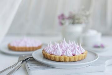 Mini tartlet with fruit jam and pink meringue. Tart with Italian meringue cream on white plate on table. Selective focus, copy space, close up view. 