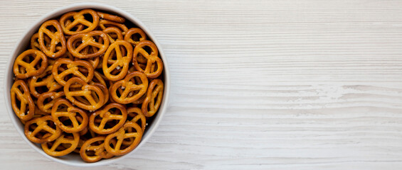 Crispy Pretzel Crackers in a Gray Bowl on a white wooden background, top view. Flat lay, overhead, from above. Space for text.