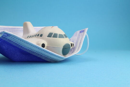 kleines Flugzeugmodel mit Schutzmaske und blauem Hintergrund steht für Reisen in Zeiten einer Pandemie