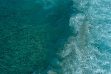 Aerial view of surfer sitting out the back of the beach, waiting for a wave, sitting on his surfboard
