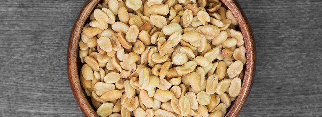 Peanuts close-up. Lots of peanuts in a wooden bowl on a wooden table. The view from the top. Banner with space for text