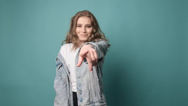 Hey you, come to me please. Young attractive woman isolated over turquoise background showing come here gesture with hand, inviting, welcoming. 
