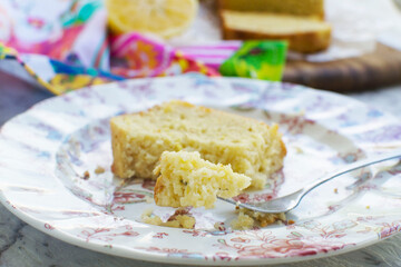 Home made cake concept. Or baking concept. A slice of vanilla or lemon cake freshly baked on a patterned plate. Someone is eating the cake with a fork. Close-up of the piece being eaten. 