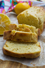 Homemade cake or baking concept. A vanilla or lemon loaf cake freshly baked and sliced on a wooden cutting board. There are lemons and a colourful tea towel in the background. 