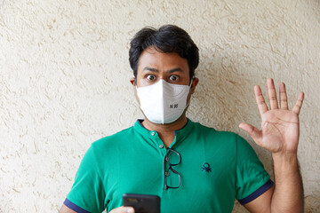 Man wearing a Green T-shirt holds a cell phone while looking surprised