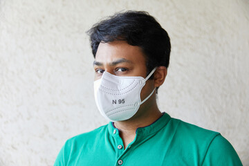 Adult Indian man wearing White N95 Mask in Green round neck T-shirt looking into the camera and looking into the camera with head faced 45 degrees