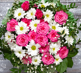 Beautiful pink roses and white daisies in a box on a gray wooden background.