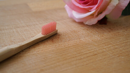 Eco-friendly bamboo toothbrush with blurred pink rose on a wood background. Natural organic dental concept