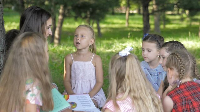 Young woman at work as educator reading book to boys and girls in park