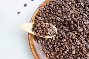 Fototapeta premium Composition in the rays of the bright sun. Beautifully roasted brown coffee beans on a round dark wood plate and on a small wooden spoon (selective focus not on all beans)