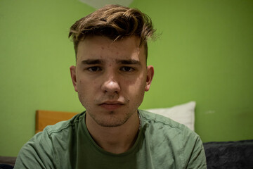 Young male with light brown hair having a worried and devastated look in his eyes in a green bedroom