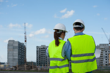 Rear View - Two Young Engineers A Man And A Woman In Green Vests And Helmets Are Discussing A Plan