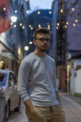 Young male with brown hair in a white long sleeve shirt in an alley with fairy lights installed