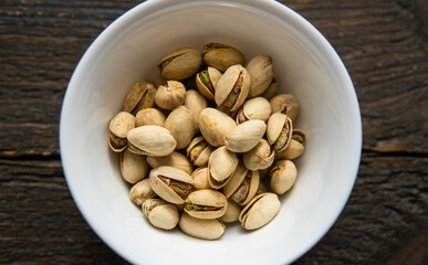 Pistachios in a small plate on a vintage wooden table. Pistachio is a healthy vegetarian protein nutritious food. Natural nuts snacks.