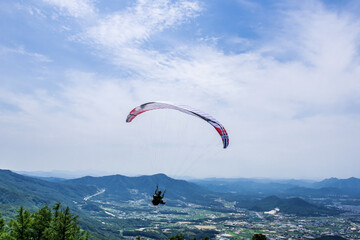 Paraglider flying against the blue sky with colorful wing above the clouds.