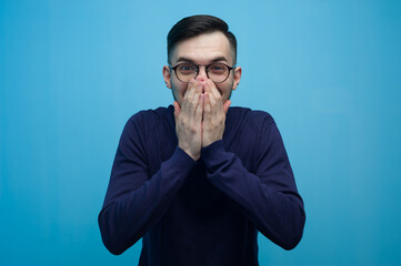 Portrait of a surprised young man in glasses and a sweater looking at the camera