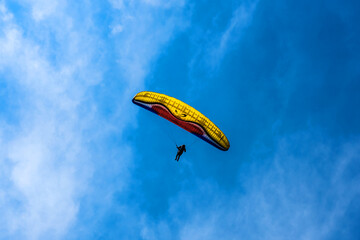 Paraglider flying against the blue sky with colorful wing above the clouds.