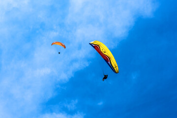Paraglider flying against the blue sky with colorful wing above the clouds.