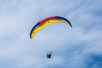 Paraglider flying against the blue sky with colorful wing above the clouds.