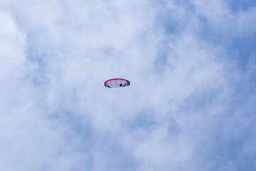 Paraglider flying against the blue sky with colorful wing above the clouds.