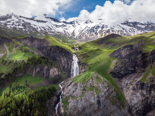 Naklejka na ściany i meble Stunning waterfall in the Swiss alps canton Berne. Aerial drone shot. Snowy mountains in the background.