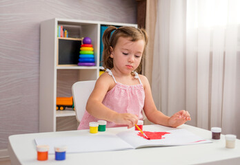 a little girl sits at a table and draws at the table with a brush and paints