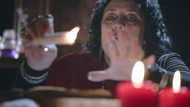 Middle-aged female psychic holds burning candle over bowl with water