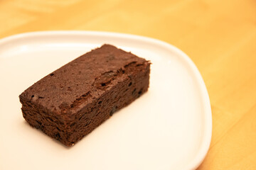 Delicious dark chocolate brownie on white plate with warm lighting at bakery shop.