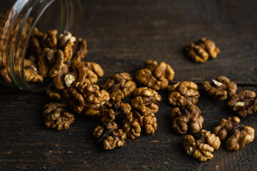 Walnut scattered on the wooden vintage table from a jar. Walnut is a healthy vegetarian protein nutritious food. Walnut kernels and whole walnuts on rustic old wood.